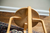 Vintage light wood stool underside, showing curved legs, screws, and natural patina.