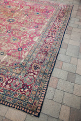 Distressed vintage Persian Kerman rug corner with intricate floral and vine borders.