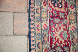 Distressed Persian Kerman rug detail, ruby red, blue, and coral curvilinear floral pattern.