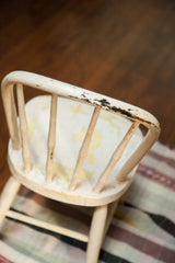 Chippy ivory white paint and dark wear on the antique child's Windsor chair back.