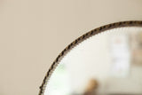 Scalloped and beveled glass edge of the antique round mirror with dark textured frame.