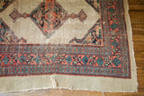 Distressed corner of Antique Persian Serab rug, showcasing worn pile, coral and teal geometric borders, and visible mending.