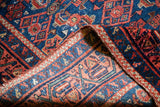 Rich indigo and terracotta Herati design with finely woven detail on a folded Malayer rug.