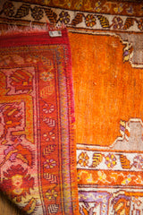 Folded vintage Turkish prayer rug edge, revealing red plainweave and rich orange pile with mauve design.
