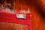 Orange pile and striped red plainweave end of a vintage Turkish rug with tag.