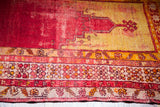 Worn red Turkish prayer rug with faded yellow mihrab and detailed floral borders.