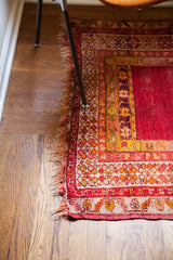 Distressed red antique Turkish prayer rug corner, tattered fringe and ornate borders.