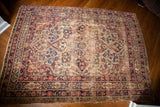 Decorative distressed corner of antique Persian Kerman rug with red, blue, and ivory floral motifs.