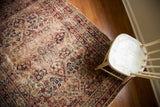 Distressed aesthetic with softened blues, reds, and floral motifs on an antique Kerman rug.