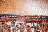 Upper border of a colorful Caucasian rug, featuring vibrant geometric motifs and time-softened pile.