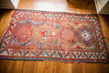 Antique Caucasian rug's worn lower corner, showing red, blue, white geometric borders.