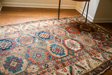 Whimsical, varied geometric medallions in blue, coral, and earth tones on an antique Caucasian tribal rug.