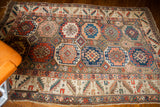 Intricate octagonal medallions in blue, red, and peach on the brown field of an antique Caucasian tribal rug.