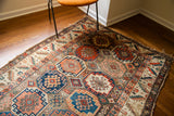 Corner of antique Caucasian tribal rug, featuring geometric borders, varied patterns, and visible fringe.
