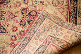 Worn antique Kerman rug corner showing blanched field, cochineal red scrolling spandrels, and foundation weave.