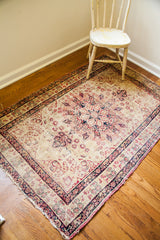 Worn antique Kerman rug corner with blanched ivory field and scrolling cochineal red patterns.