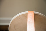 Alvar Aalto style stool's curved top, chipped ivory paint, rising orange leg.