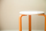 Glossy white curved seat edge and chipped orange leg of vintage stool.