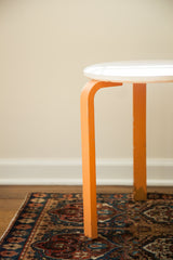 Chipped orange legs of a Mid Century Alvar Aalto style stool over a vintage patterned rug.