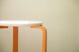 Mid century Aalto style stool's curved ivory top and chipping orange leg.
