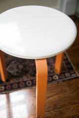 Vintage Mid Century stool with chipped orange paint on its curved leg.