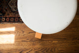 Round top of the Alvar Aalto style stool, showcasing chipped ivory paint and orange leg.
