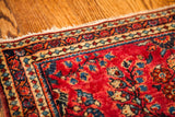 Vintage Sarouk Persian rug corner, featuring ruby red field, blue floral design, and intricate borders.