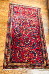 Vintage red Sarouk rug corner featuring crisp floral medallion and intricate border details.