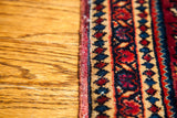 Finely detailed border of the vintage Sarouk rug with saturated red, blue, and tan motifs.