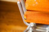 Close-up of vintage Pirelli Castelli chair armrest, vibrant orange fabric with corner wear.