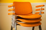 Stacked Pirelli DSC chairs, highlighting orange textured upholstery and aluminum armrests.