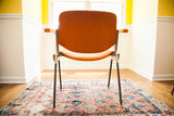 Vintage orange Pirelli chair back on a worn red and blue geometric patterned rug.