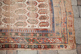 Distressed antique Caucasian rug corner with ivory field, boteh, and colorful geometric borders.