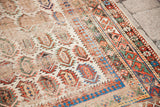 Distressed antique Caucasian rug detail with ivory field, colorful boteh, and geometric border.