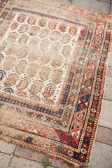 Distressed ivory field with boteh motifs and geometric borders of a Caucasian rug.