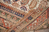 Folded antique Caucasian rug showing distressed geometric boteh patterns and woven foundation.