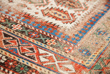 Distressed antique Caucasian rug detail with vibrant geometric patterns in red, blue, and ivory.