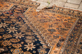 Torn fringe and geometric patterns on the earth-toned end of an antique tribal rug.