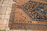 Frayed corner of an antique Southwest Persian tribal rug, showing dark blue and earth-toned geometric patterns.