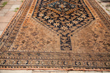 Antique Southwest Persian rug's lower end, with geometric earth tones, navy field, and a tear.