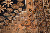 Antique Southwest Persian rug featuring geometric tribal patterns in earth tones and navy, showing a tear.
