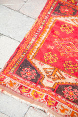 Textured corner of a vintage red Turkish Yastik rug with angular patterns and fringe.