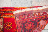 Folded vintage Turkish Yastik rug showing rich red geometric patterns, weave, and ivory fringe.