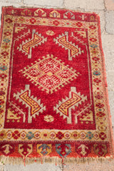 Lower geometric border, deep red field, blue accents, and frayed fringe on vintage Turkish rug.