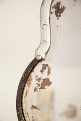 Distressed white paint peeling on a mirror's beveled edge, revealing weathered wood.