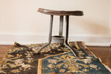 Antique industrial galvanized steel milking stool with curved seat and splayed legs.