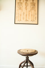 Antique industrial wooden stool with a distressed beige seat, leather trim, and dark wood-iron base.