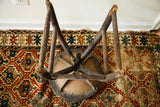 Inverted antique industrial wooden stool showing rustic legs and iron seat base.