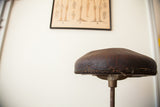 Cracked brown leather seat and original nail-back trim of the antique medical stool.