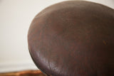 Close-up of the medical stool's aged, dark brown leather seat with visible cracking.